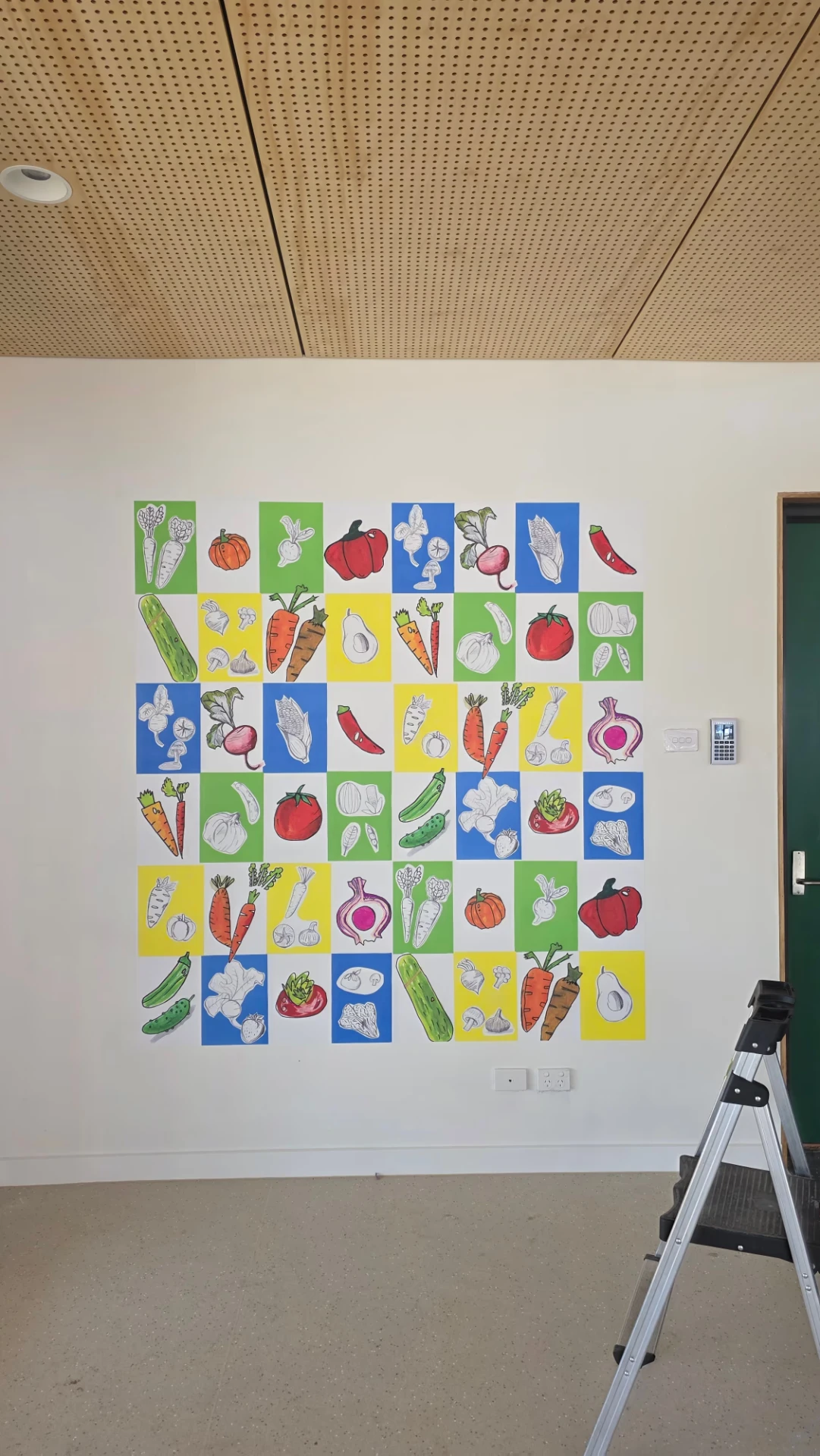 Grid of colourful printed vegetable artwork panels installed on a school interior wall
