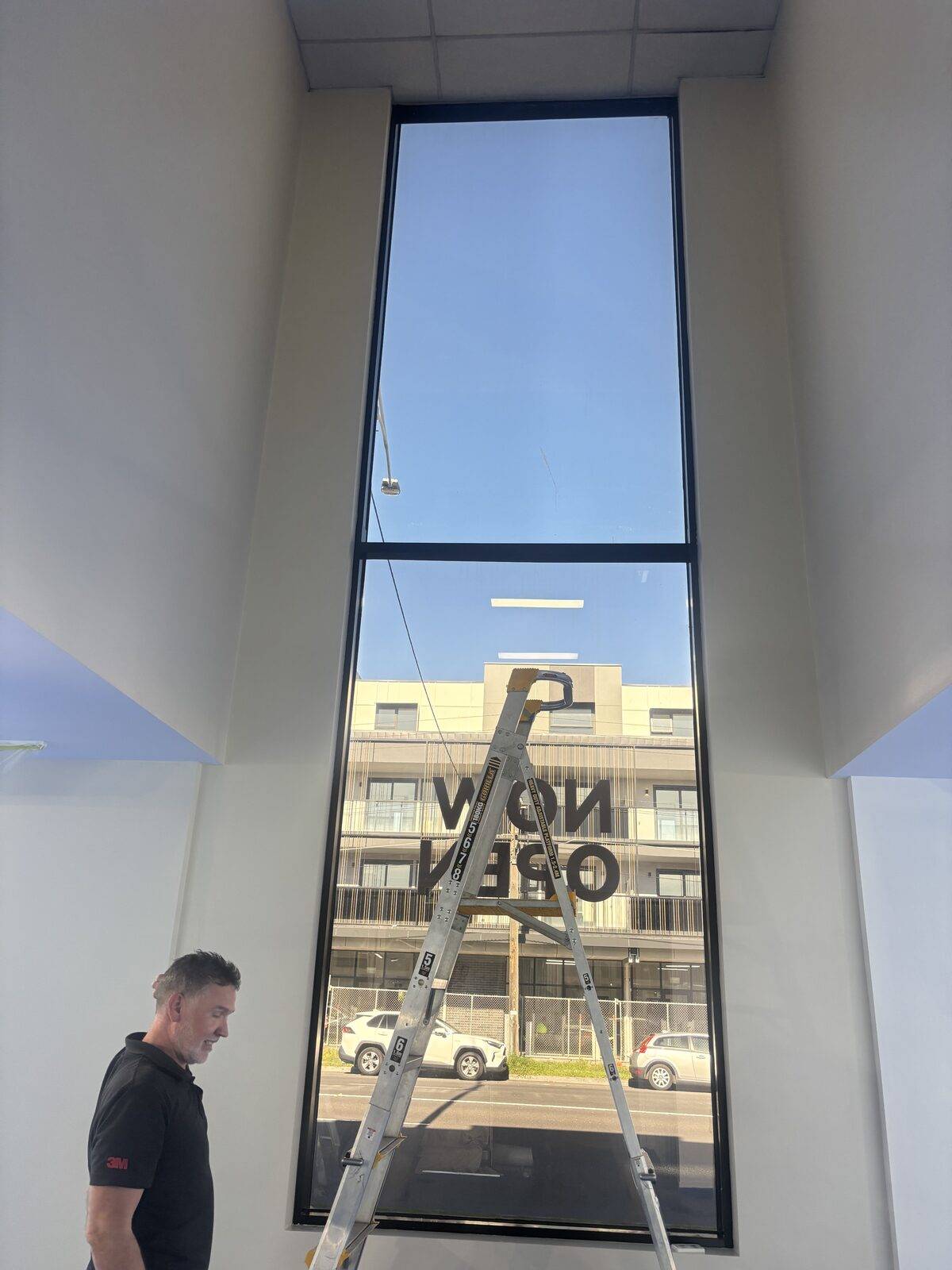 Tall Melbourne shopfront window before 3M security film installation, reverse 'NOW OPEN' decal visible from inside