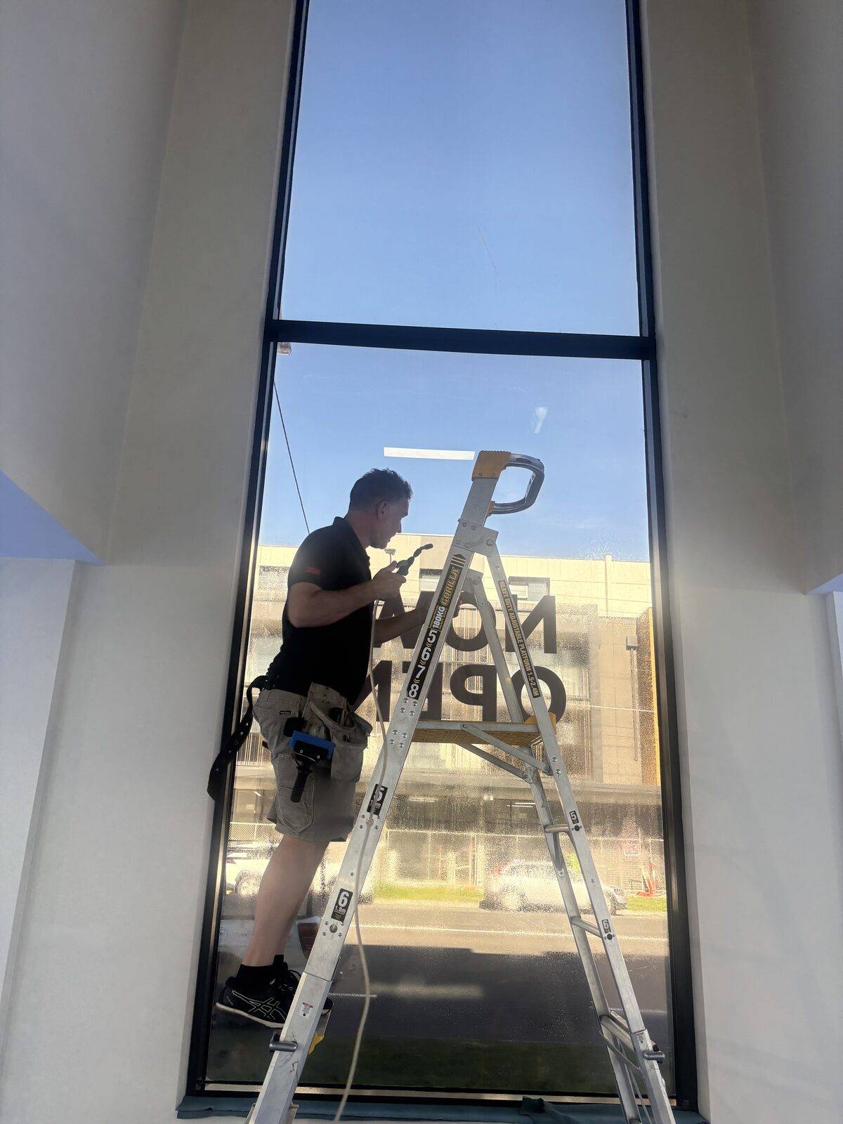 UV Window Coatings installer on a ladder applying 3M Ultra S800 security film to a 3.2m tall Melbourne shopfront window