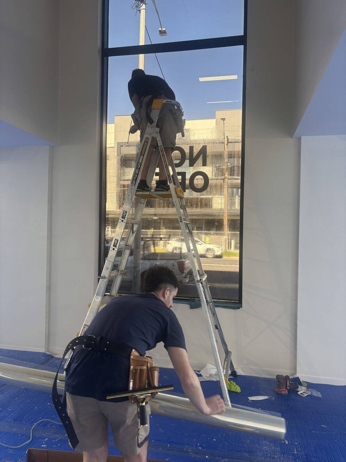 Two UV Window Coatings installers squeegeeing 3M Ultra S800 security film onto a large Melbourne shopfront window